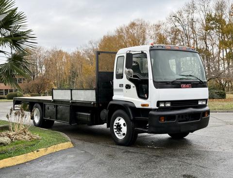 A white 2007 GMC F7500 flatbed truck is parked with a black flatbed and a metal side rail