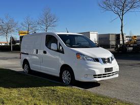 A white 2017 Nissan NV200 van parked on the street with a clean design and compact size
