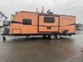 A 2015 Winnebago Of Indiana Travel Trailer in orange with black accents featuring a streamlined design and dual axles