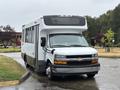 A white 2020 Chevrolet Express bus with a large front windshield and side windows parked on a wet surface