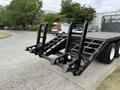 A black Freightliner FL80 flatbed truck with ramp attachments and large rear wheels is parked on a paved surface