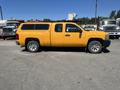 A yellow 2013 Chevrolet Silverado 1500 with a fitted canopy parked on a lot with other vehicles in the background
