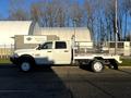 A white 2014 RAM 5500 flatbed truck with a dual wheel setup and a metal bed is parked on a paved surface