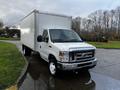 A 2019 Ford Econoline white delivery van with a large box cargo area and a spacious cabin parked on a wet road