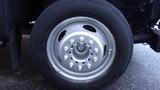 A close-up of a silver wheel with a black tire featuring multiple lug nut holes and a smooth rim surface