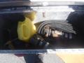 A yellow plastic container alongside metal parts and hoses inside a trailer storage compartment