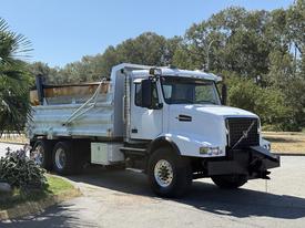 A 2005 Volvo VND dump truck with a silver cargo bed and front-mounted blade parked on a road