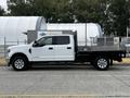 A white 2020 Ford F-350 with a flatbed and metal side rails parked on a roadway
