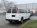 A 2016 GMC Savana van in white with a long body and tinted rear windows parked at an industrial site