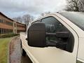 A white 2017 Ford F-350 Super Duty truck parked with its side mirror reflecting light and raindrops on its surface