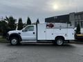 A white 2009 Ford F-550 utility truck with a flatbed and storage boxes on the sides