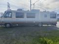 A 1987 Chevrolet Fleetwood Pace Arrow recreational vehicle parked with a cream-colored exterior and blue and brown stripes along the side