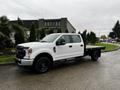 A white 2020 Ford F-350 Super Duty with a flatbed truck design parked on a road