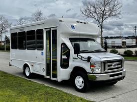 A 2016 Ford Econoline bus with a white exterior and large windows designed for accessibility with a wheelchair ramp on the side