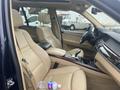 Interior of a 2009 BMW X5 featuring beige leather seats with a water bottle on the center console and a black tablet resting on the front seat