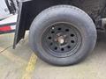 A close-up of a black tire on a wheel with multiple holes and a rusted hub showcasing a branding name on the sidewall