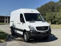 A white 2017 Mercedes-Benz Sprinter van with a high roof and distinctive front grille is parked at an angle showcasing its large cargo area and black accents on the lower body