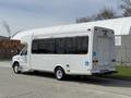 A white 2010 Ford Econoline shuttle bus with large windows and a wheelchair accessibility symbol on the side