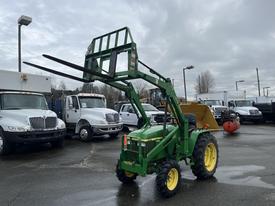 A green 2003 John Deere 790 tractor equipped with a front loader and forks raised for lifting equipment or materials