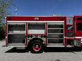 A 2006 Emergency One Fire Truck with open storage compartments on the side showcasing a metal interior and red wheels