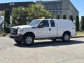 A white 2014 Ford F-250 SD pickup truck with a truck cap parked on a paved surface under bright sunlight