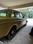A yellow 1978 Volvo 244 parked in a garage showing its side profile and rear features with a black tire and chrome accents
