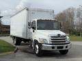 A 2017 Hino 338 box truck with a white exterior and a silver front grille parked on the road with a large cargo area in the back