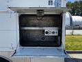A 2004 Freightliner M2 truck's storage compartment is open showing the empty interior with a metal shelf and gauges mounted on the back wall