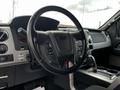 Interior view of a 2014 Ford F-150 showing the steering wheel and gear shift with various control buttons and instruments visible on the dashboard