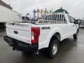 A white 2017 Ford F-250 Super Duty pickup truck with a flatbed and a ladder rack on the back showcasing the 4x4 badge