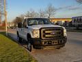 A 2012 Ford F-250 pickup truck with a white body and black front grille parked on the side of the road