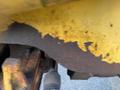 Close-up of the rusty undercarriage of a 2007 Komatsu WB156PS-5 construction machine showing peeling paint and wear on the surface