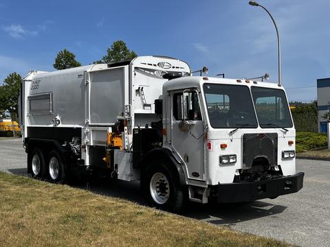A 2010 Peterbilt 320 garbage truck with a white body and black chassis featuring a side-loading compactor and visible hydraulic systems