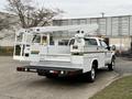 A 2001 Ford F-350 truck with a white body and a utility bed featuring a raised aerial lift and safety barriers