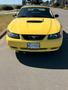 A bright yellow 2003 Ford Mustang is parked with a front view showcasing its distinctive grille and hood scoop