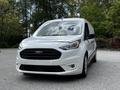 A 2019 Ford Transit Connect in white with a black grille and headlights parked in a well-lit area