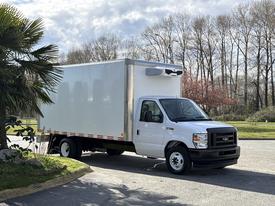 A 2023 Ford E-450 box truck in white with a refrigeration unit on top parked at an angle with a clean and modern design