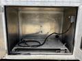 An open metal storage compartment showing a smooth interior with a power cable and a hole on one side