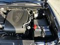 The engine compartment of a 2021 Toyota Tacoma featuring a V6 engine cover and a battery with a red terminal and several cables