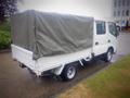 A white 2003 Toyota Toyoace truck with a covered cargo bed is parked, featuring a green tarp over the rear portion of the truck