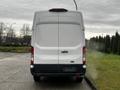 A white 2021 Ford Transit van is parked facing away with its rear doors closed