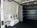 A white 2017 Ford Transit van interior with metal shelving units on the right side and an unfinished wall section on the left