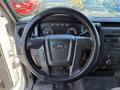 A 2014 Ford F-150 steering wheel with controls and dashboard displays visible in the foreground