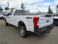 A 2017 Ford F-250 SD pickup truck with a white exterior and a flatbed featuring a metal frame for cargo transport