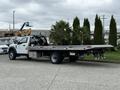 A 2022 Ford F600 flatbed truck with a silver flatbed design and a black cab parked with palm trees on the flatbed