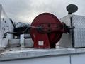 A red hose reel mounted on a vehicle with silver diamond plate storage and a tire visible in the background