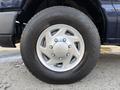 A close-up of a silver wheel and tire from a 2011 Ford Econoline with the Ford logo and detailed tire tread pattern visible