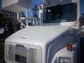 A white 2006 Freightliner FS65 bus with a prominent front grille and large windshield featuring side mirrors and a raised platform on the roof