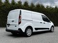 A 2019 Ford Transit Connect van in white with black accents parked with its side facing the viewer and rear doors closed