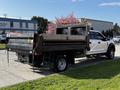 A 2021 Ford F-550 medium-duty truck with a dump bed in a white and black color scheme, featuring safety lights and a metal mesh back panel